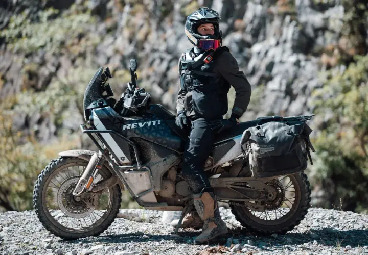 Motociclista con equipo **waterproof** listo para la aventura. ¿Será **Gore-Tex**? La moto, su compañera en terrenos difíciles.