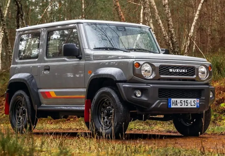 Szary Suzuki Jimny 2026 z kolorowymi pasami na boku, gotowy na terenową przygodę w lesie.