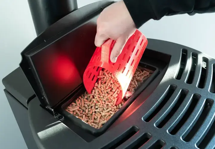 Ręka wsypuje pellet do zasobnika czarnego pieca na pellet.