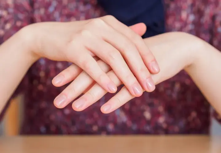 Dłonie z naturalnymi paznokciami, delikatnie skrzyżowane. Choć manicure japoński ma wiele zalet, warto pamiętać o jego potencjalnych wadach.