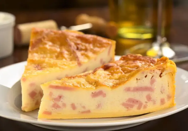 Deux parts de quiche jambon fromage dorée sur une assiette blanche, avec un verre de vin en arrière-plan.