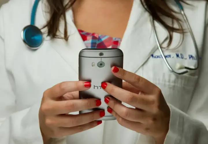 Lekarka w białym kitlu z czerwonymi paznokciami trzyma telefon. Czy pracodawca widzi kod choroby na ekranie?