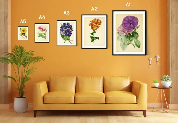 Un sofá amarillo bajo un marco din A3 con flores moradas y rosadas.