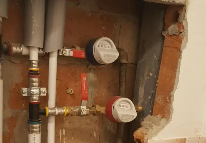 Instalacja wodna z dwoma licznikami i czerwonym zaworem.