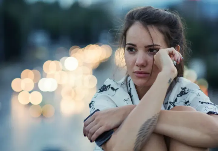 Giovane donna pensierosa, con luci sfocate sullo sfondo, sembra voler rimuovere ricordi traumatici.