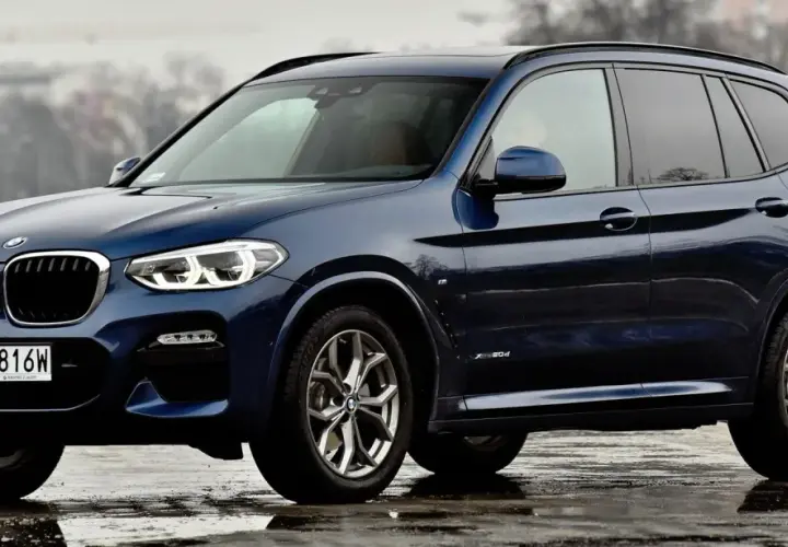 Ciemnoniebieskie BMW X3 na mokrej nawierzchni. Eleganckie linie i sportowy charakter tego SUV-a robią wrażenie.