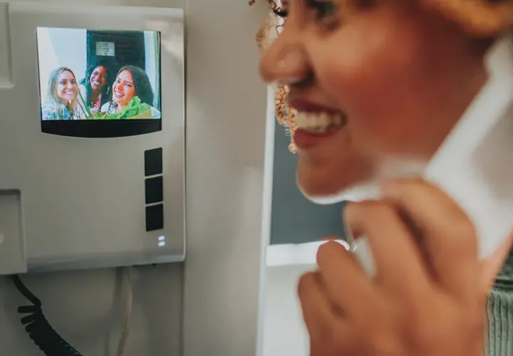 Instalación de telefonillos: mujer sonríe mientras habla por el intercomunicador, viendo a sus amigas en la pantalla.