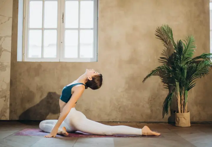 Mujer realiza un profundo estiramiento psoas en una esterilla de yoga, con la espalda arqueada y la cabeza echada hacia atrás.