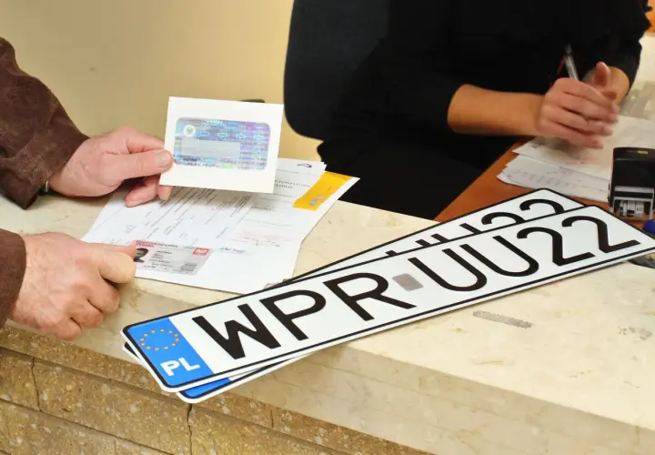 Ręce klienta pokazują dokumenty i nowe tablice rejestracyjne WPR UU22, gotowe do odbioru po załatwieniu formalności.