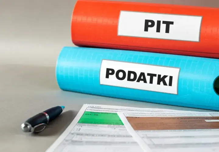 Dwa segregatory z napisami "PIT" i "PODATKI" oraz formularze podatkowe i długopis. Czas na ulgę podatkową!
