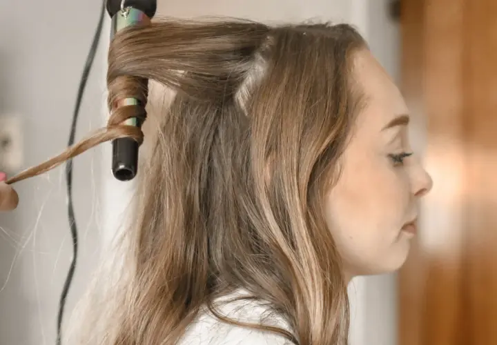 Creando peinados fáciles y rápidos: una mano riza el cabello de una mujer con una plancha.