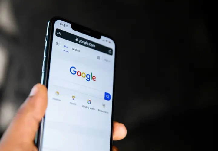 Dłoń trzyma smartfon z otwartą stroną Google. Widać pasek wyszukiwania i opcje takie jak pogoda, sport, filmy, restauracje, idealne do odkrywania treści w Google Discover.