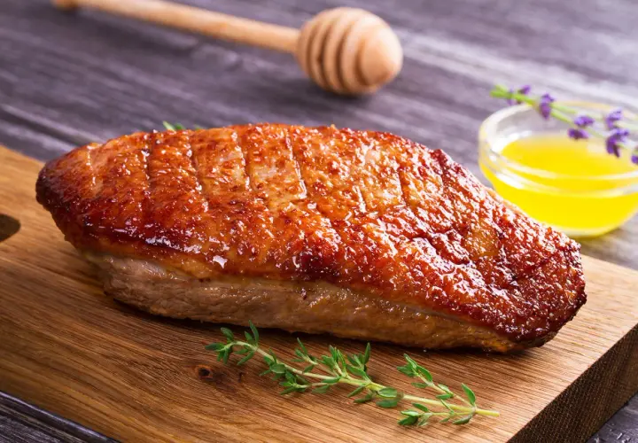 Un magret de canard au barbecue, la peau croustillante et dorée, prêt à être dégusté avec une touche de miel et de thym.