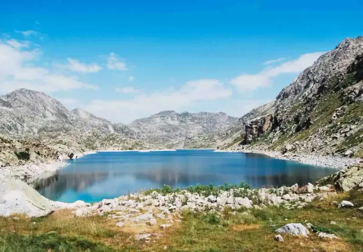 Un lago azul profundo en la vall fosca que ver, rodeado de montañas rocosas y cielo azul con nubes.
