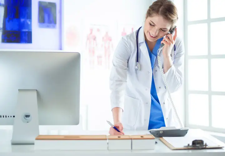 Medico al telefono, impegnato nella gestione appuntamenti, mentre scrive su un blocco note.