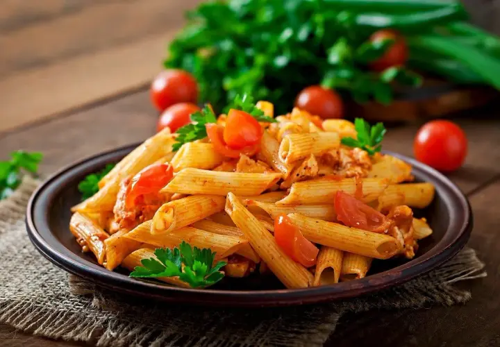 Penne z sosem pomidorowym i kurczakiem, ozdobione pomidorkami i natką pietruszki. Idealne pytanie: jakie wino do spaghetti?
