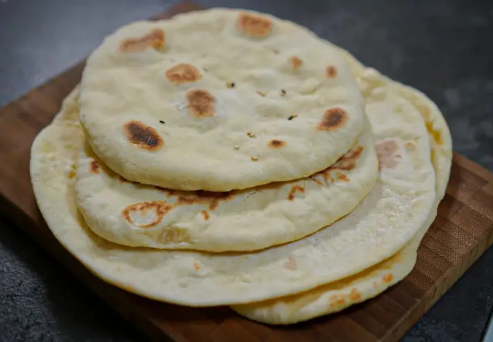 Pile de pains arabes moelleux, légèrement dorés par la cuisson, sur une planche en bois. Parfait pour accompagner un repas.