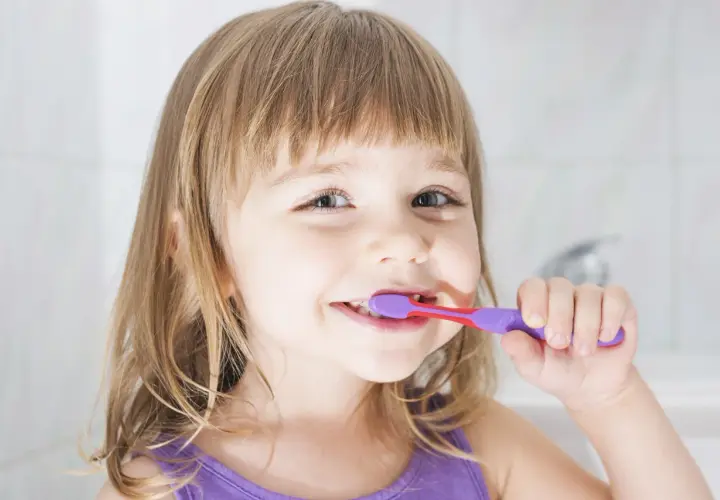 Bambina sorridente si lava i denti con un dentifricio al fluoruro di sodio per un sorriso smagliante.