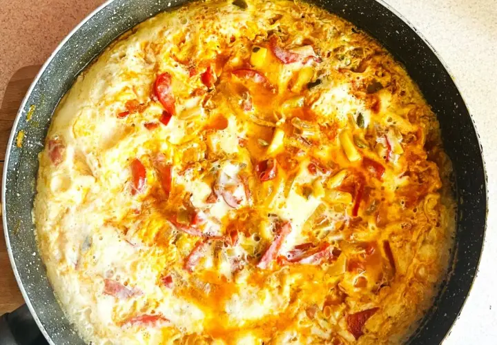 Pyszny omlet z warzywami w trakcie smażenia na patelni. Widoczne kawałki papryki i cebuli.