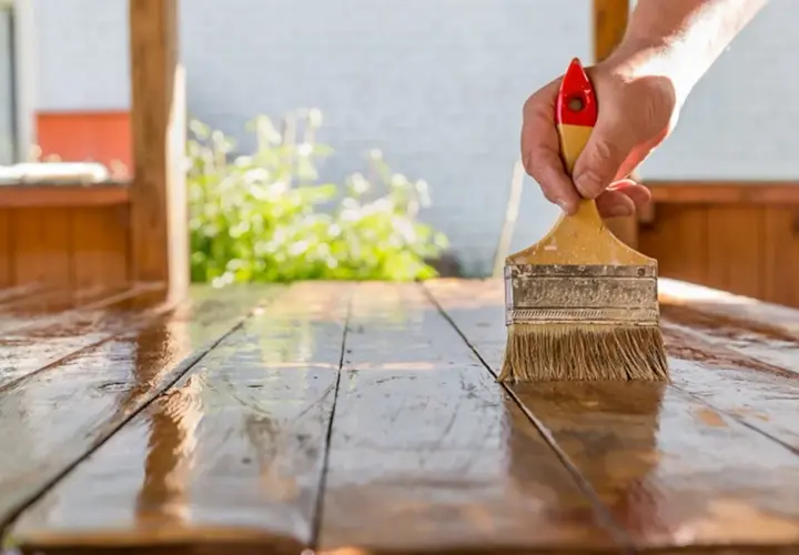Mano aplicando barniz a una mesa de madera. El proceso de lijar después de barnizar es clave para un acabado perfecto.