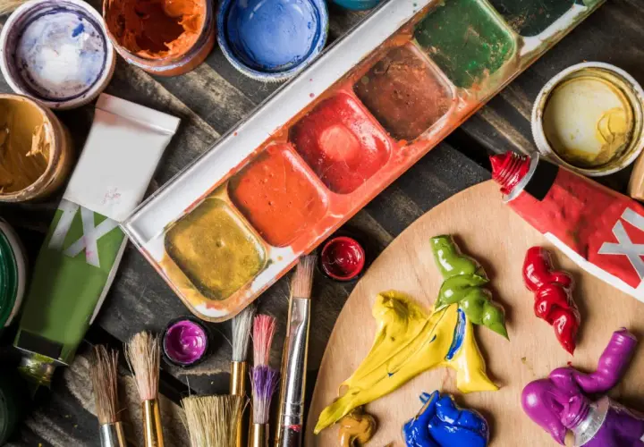 Palette d'un artiste peintre acrylique avec tubes de peinture, pinceaux et godets de couleurs vives sur fond de bois.