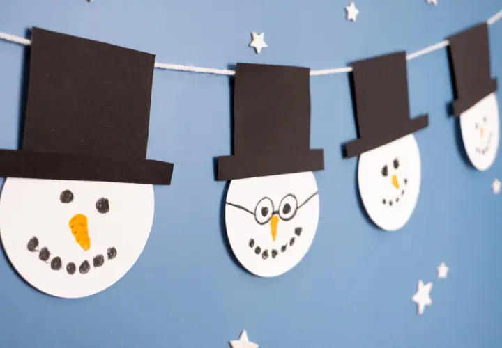 Schneemann-Girlande als winter bastelideen kinder. Weiße Kreise mit schwarzen Hüten und Gesichtern hängen an einer Schnur.