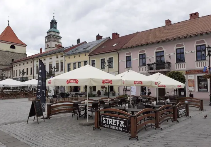 Letni ogródek kawiarniany na rynku w Żywcu. Parasole z logo Żywiec, stoliki i ławki. W tle kamienice i wieża ratuszowa.