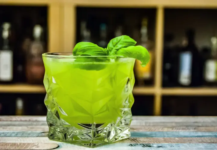 Orzeźwiający drink z likierem miętowym, ozdobiony listkami bazylii, w szklance o geometrycznym kształcie.