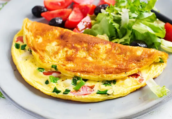 Złocisty omlet z warzywami i sałatką na talerzu.