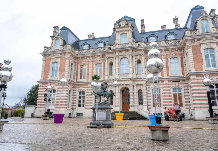 Devant un château, des sphères argentées, comme des habits de lumière, scintillent sur des structures métalliques, entourant une statue équestre.