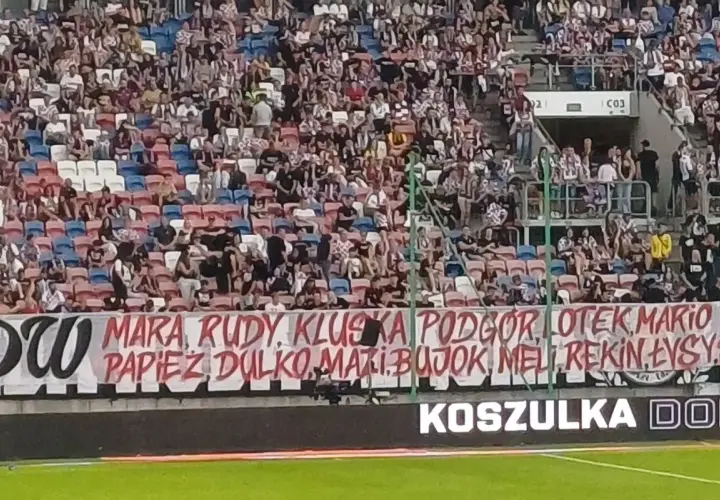 Tłum kibiców na trybunach, transparent z nazwiskami piłkarzy i hasłem "torcida".