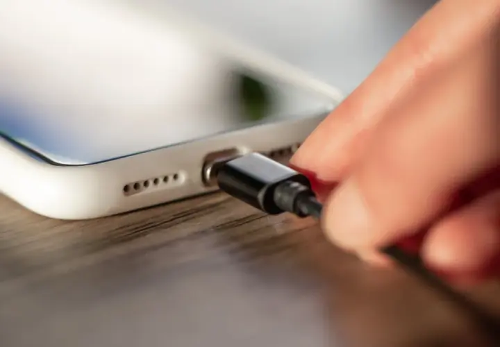 Dłoń podłącza kabel do białego smartfona. Zastanawiasz się, ile wynosi gwarancja na to urządzenie?