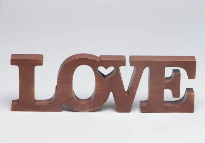 Letras de madera marrón forman la palabra "LOVE", con un corazón tallado en la "O".