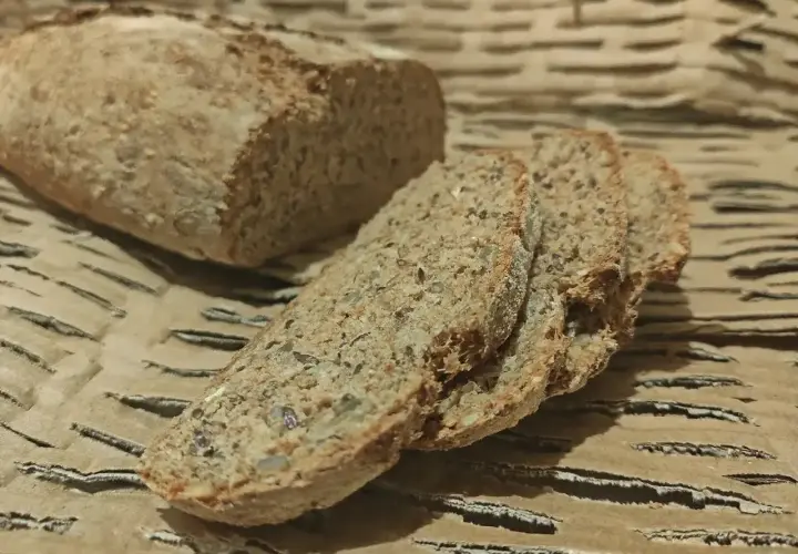 Chleb orkiszowy, pokrojony w kromki, z widocznymi ziarnami, leży na falistej tekturze.