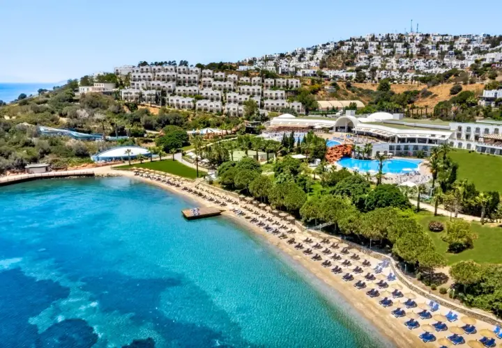 Widok na hotel Yasmin Bodrum Resort z plażą, basenami i białymi budynkami na wzgórzu. Idealne miejsce na wakacje, jak sugerują yasmin bodrum resort opinie.