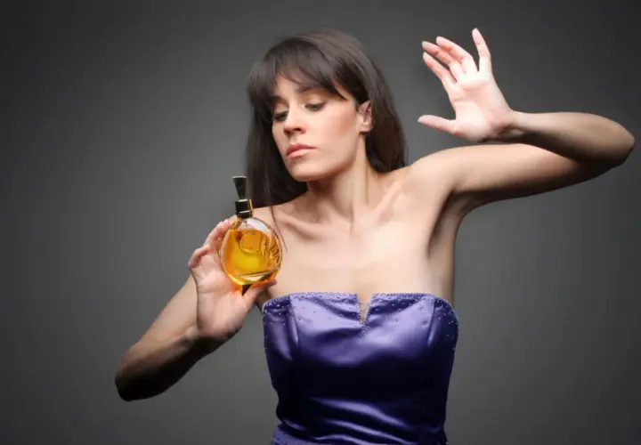 Kobieta w fioletowej sukni trzyma buteleczkę perfum.