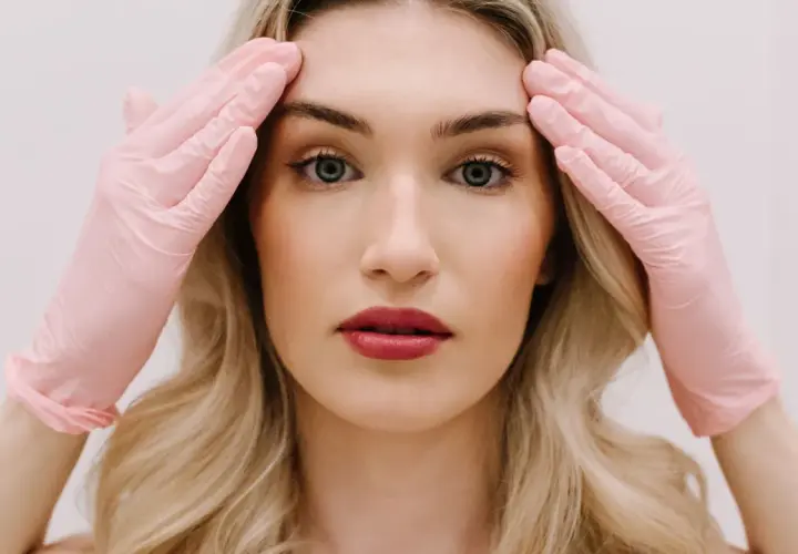 Kobieta w różowych rękawiczkach dotyka skroni, przygotowując się do zabiegu face lifting.