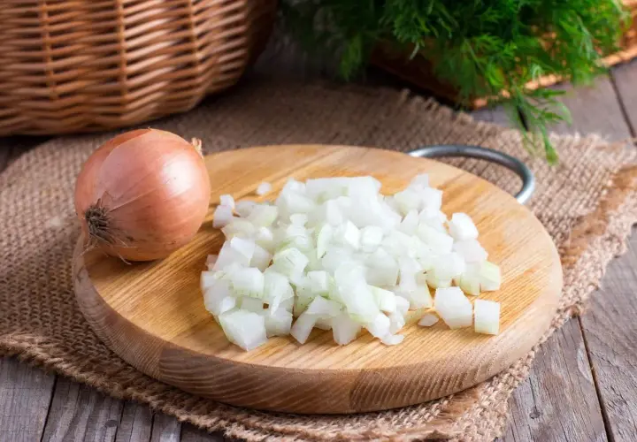 Cipolla intera e tritata su tagliere di legno. Un rimedio naturale per come togliere l'odore di aglio dalla bocca.