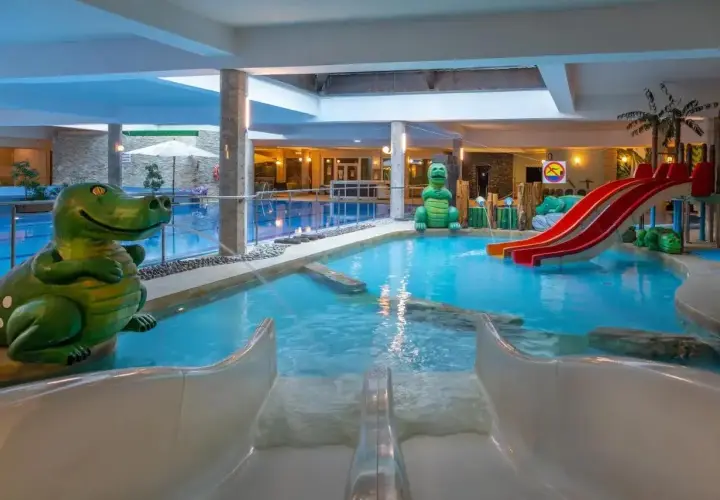 Wesoły hotel z aquaparkiem zaprasza do zabawy! Dwa zielone dinozaury pilnują basenu ze zjeżdżalniami.