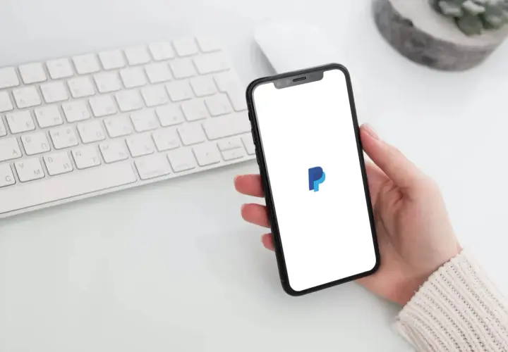 Dłoń trzyma smartfon z logo PayPal, obok klawiatura. Zastanawiasz się, czy PayPal jest darmowy?