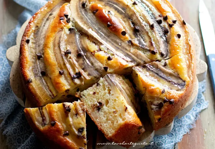 Delizioso dolce con banane e gocce di cioccolato, tagliato a fette su un tagliere di legno.