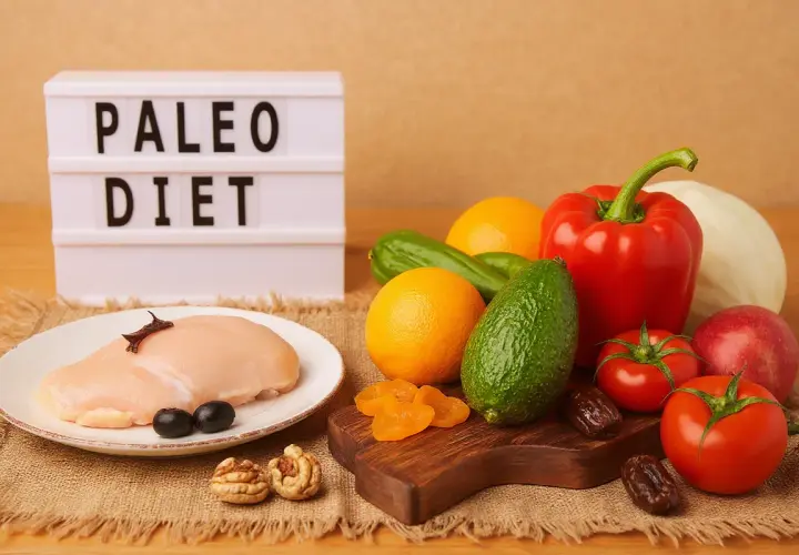 Dieta paleo co to? Na stole surowy kurczak, warzywa, owoce, orzechy i daktyle.