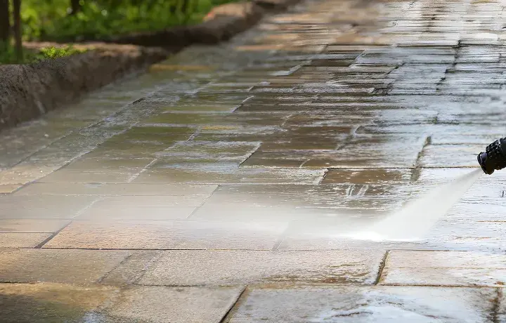 Hochdruckreiniger säubert ein Betonpflaster. Der Wasserstrahl entfernt Schmutz und lässt die Steine wieder wie neu aussehen.
