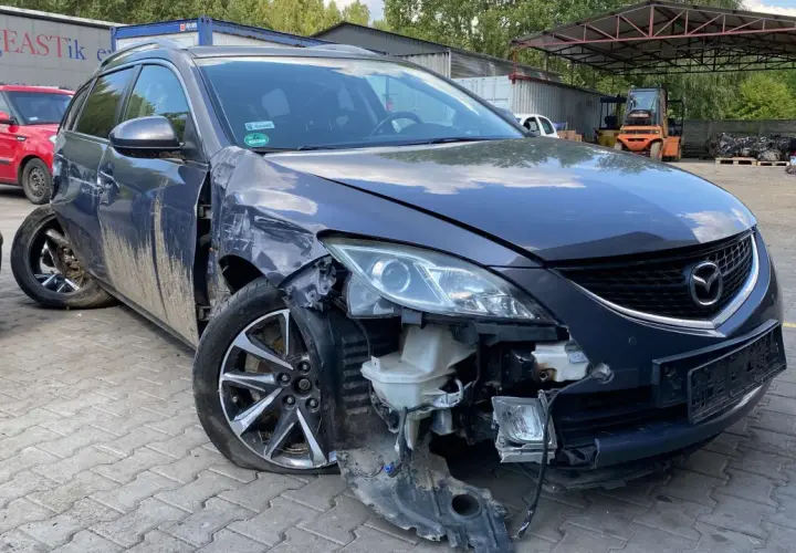 Uszkodzona Mazda na złomowisku, z urwanym zderzakiem i przebitą oponą. Może to być początek procesu, jak zezłomować samochód.
