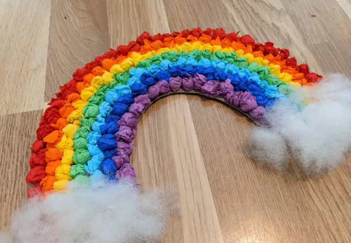 Ein bunter Regenbogen, gebastelt aus zerknülltem Krepppapier in allen Farben, mit flauschigen Wolken aus Watte.
