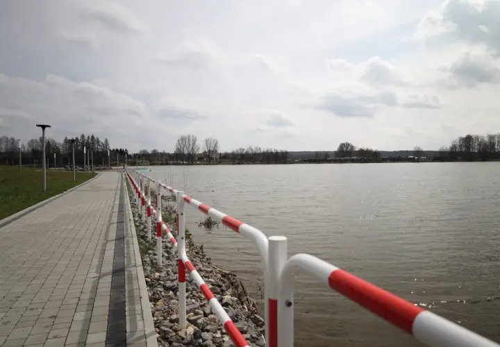 Spacerem nad zalewem wolbromskim, z czerwono-białą barierką i brukowaną ścieżką.