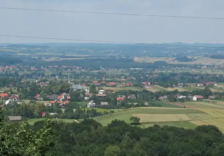 Widok na malowniczą wieś Przytkowice z kościołem w centrum, otoczoną zielonymi polami i lasami.