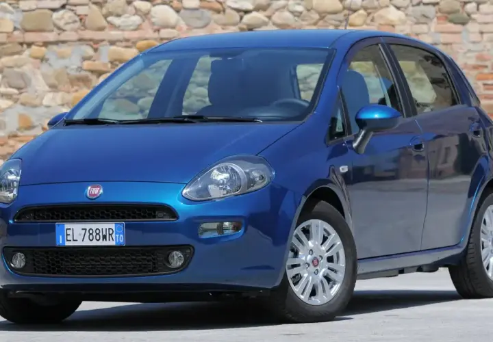 Una Fiat Punto blu brillante parcheggiata davanti a un muro di pietra.