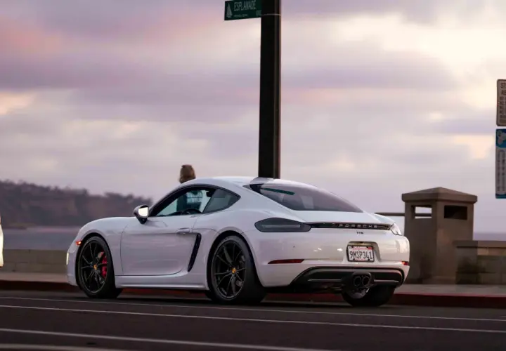 Białe Porsche GT4 z czerwonymi zaciskami hamulcowymi stoi przy drodze z widokiem na ocean.