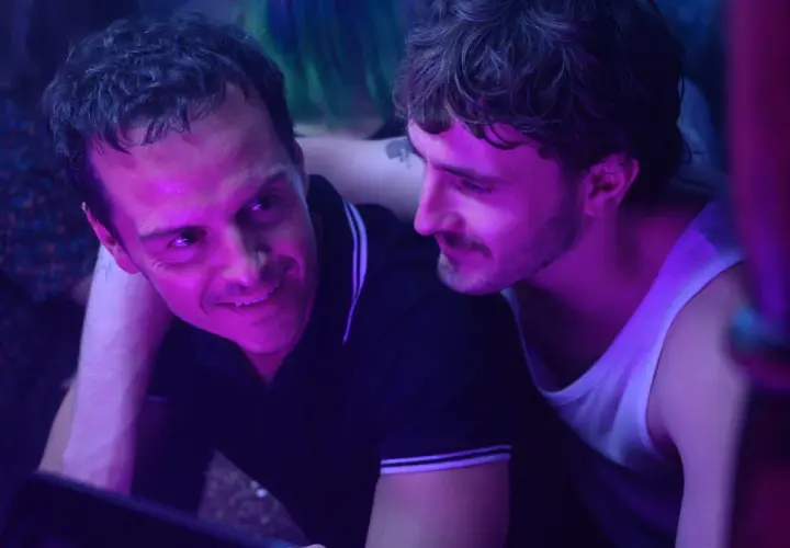 Dwóch mężczyzn w klubie, jeden z nich uśmiecha się do drugiego. To scena z filmu "Dobrzy nieznajomi", która zasługuje na recenzję.